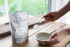 a person holding a spoon in front of a bag of milk paint on a wooden table