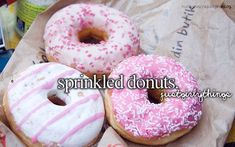 three donuts with pink frosting and sprinkles are on a wrapper