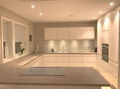 an empty kitchen with all white cabinets and counter tops, lights on above the sink