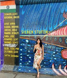 a woman is standing in front of a wall painted with different colors and designs on it