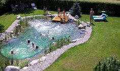 people are playing in an outdoor pool with rocks and stones on the ground, surrounded by grass