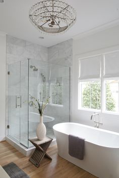 a white bath tub sitting under a chandelier in a bathroom next to a window