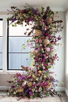 an arrangement of flowers on the floor in front of two large windows, with a rug underneath it