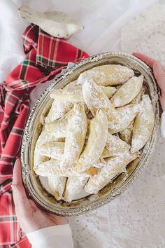 a person holding a bowl filled with powdered sugar covered pastries on top of a table