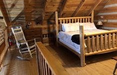 a bed in a room with wooden floors and walls, next to a rocking chair