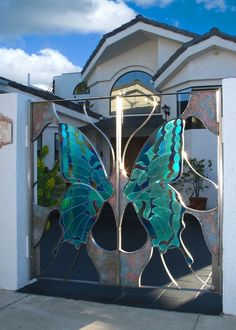 an open gate with a butterfly painted on the front and side panels, in front of a white house