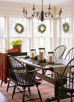 a dining room table with chairs and wreaths on the windowsill