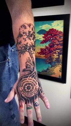 a person's hand with a tree and compass tattoo on it, in front of a painting