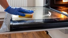 a person in blue gloves is cleaning an oven with a sponge and soap on it