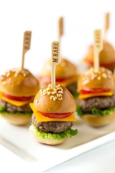 mini cheeseburgers with tiny toothpicks on them sitting on a white plate