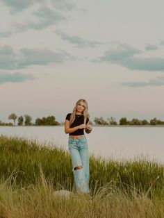 a woman standing in tall grass next to a body of water