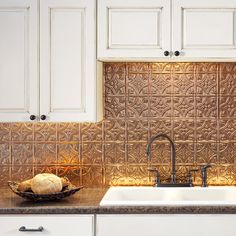 a kitchen with white cabinets and black counter tops has an intricate metal tile design on the backsplash