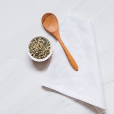 a wooden spoon sitting next to a white bowl filled with green tea on top of a white napkin