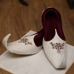 a pair of white slippers sitting on top of a wooden table next to a red shoe