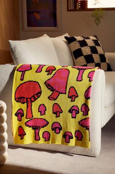 a yellow blanket with pink mushrooms on it sitting next to a white couch in a living room