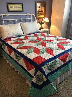 a bed with a quilt on top of it in a bedroom next to a lamp