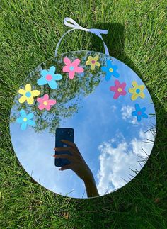 a hand holding a cell phone in front of a round mirror with flowers on it