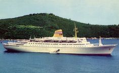 a large white boat floating on top of a lake next to a lush green hillside