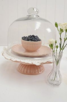 blueberries are in a bowl under a glass dome on a cake stand with flowers