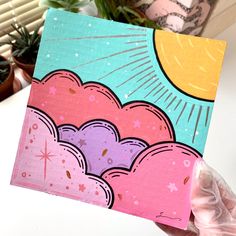 a hand holding up a card with an image of the sun and clouds on it