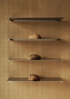 three metal shelves with bread on them against a wall in a room that has tiled walls