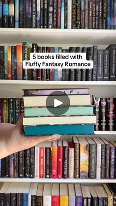 a person holding a stack of books in front of a book shelf filled with books