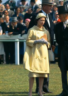 a woman in a yellow coat and hat standing next to a man wearing a suit