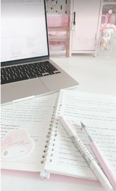 a laptop computer sitting on top of a desk next to a notepad and pen