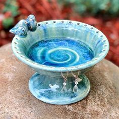 a blue bowl sitting on top of a rock with two birds perched on the rim