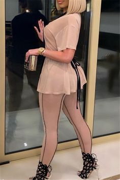 a woman in tights and heels standing by a glass door with her hand out