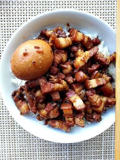 a white bowl filled with meat and rice on top of a wooden table next to a piece of bread