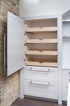 an empty pantry with white cupboards and drawers in front of a brick wall behind it