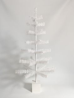 a small white christmas tree on a stand against a white background with room for text