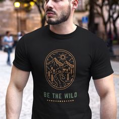 Introducing our latest t-shirt design for the adventurous souls out there! Our "Be the Wild" tee features a retro graphic of an SUV driving down a scenic road through the mountains and trees with a sunset in the background. Perfect for nature lovers, hikers, campers, explorers, and overlanders alike, this shirt will inspire you to embrace your wild side and explore the great outdoors!  Made with high-quality materials and designed for comfort, this tee is a must-have for anyone looking to add a Black Hiking T-shirt With Letter Print, Black T-shirt For Hiking With Letter Print, Black Letter Print T-shirt For Hiking, Black Graphic Tee For Camping, Black Crew Neck T-shirt For Camping, Outdoor Black Shirt With Screen Print, Black Graphic Print Shirt For Outdoor Activities, Black Graphic Print T-shirt For Camping, Black Screen Print Shirt For Outdoor