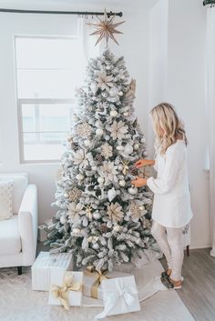 a woman decorating a christmas tree with white and gold ornaments on it in her living room