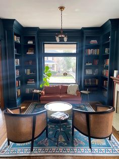 a living room with two chairs and a table in front of a window filled with books