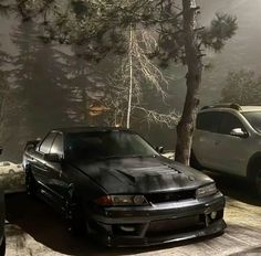 two cars parked next to each other in front of some trees and foggy sky