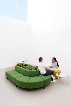 two people sitting on green couches in an empty room