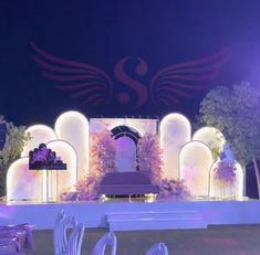 an outdoor stage set up with white chairs and purple flowers on the front, surrounded by lights