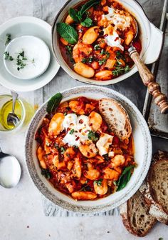 two bowls filled with pasta and sauce on top of a white table next to bread