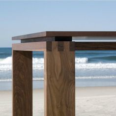 a wooden table sitting on top of a sandy beach next to the ocean with waves coming in