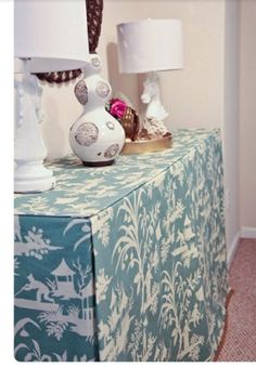 two lamps are on top of a table with a blue and white cloth draped over it