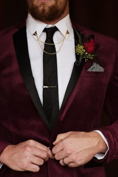 a man wearing a burgundy velvet suit with a black tie and flower boutonniere