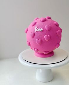 a pink ball with hearts on it sitting on top of a white cake plate