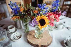 flowers are in vases sitting on a table with plates and cups around it,