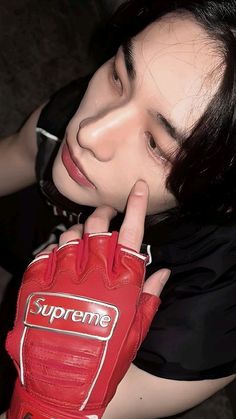 a woman in black shirt and red gloves with finger on her face next to a hand that says supreme