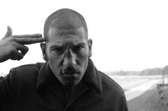 black and white photograph of a man holding his finger up to his forehead while looking at the camera