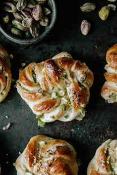 several rolls with different toppings sitting on a table next to a bowl of pistachio