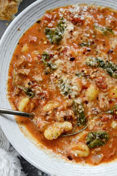 a white bowl filled with pasta and spinach soup on top of a marble table