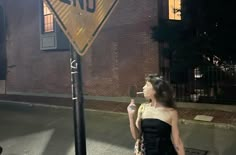 a woman standing next to a yellow and black street sign on the side of a road